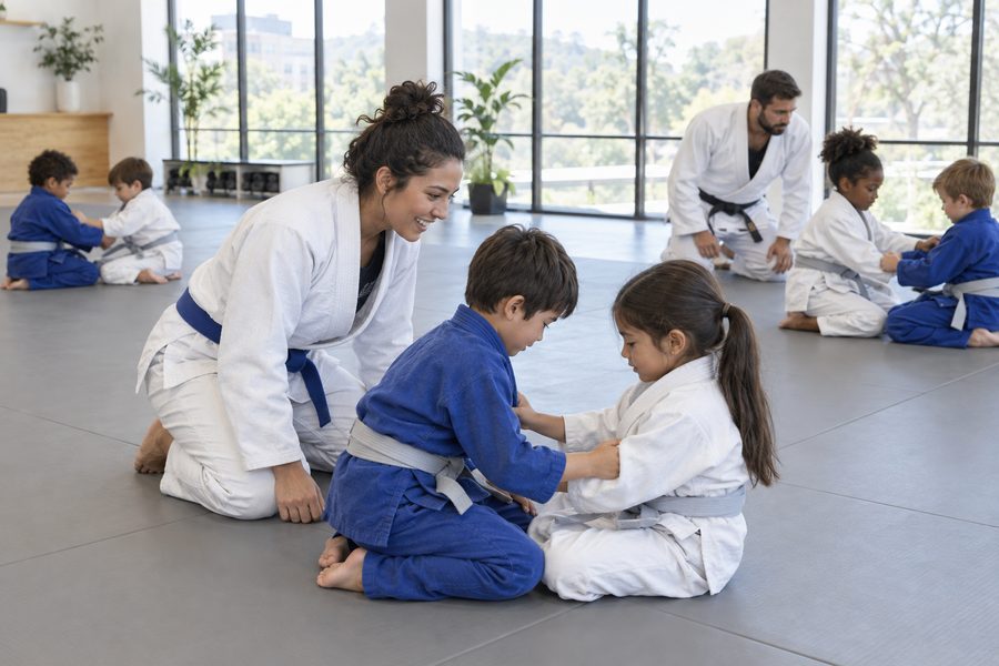 Two coaches supervising kids practicing a technique in pairs on the mats
